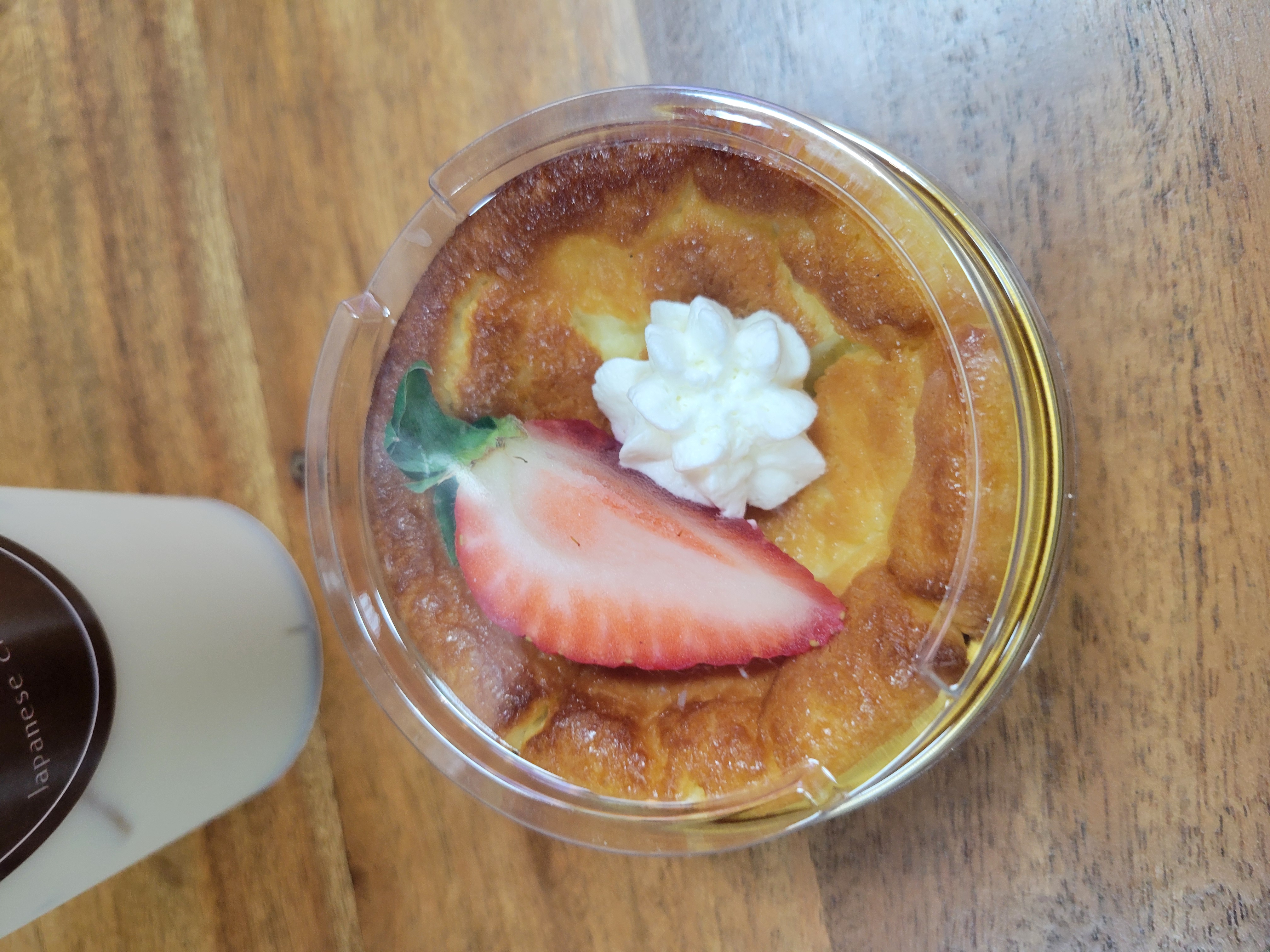Mini Japanese cheesecake with a slice of strawberry and mini whipped cream on top next to paper cup.